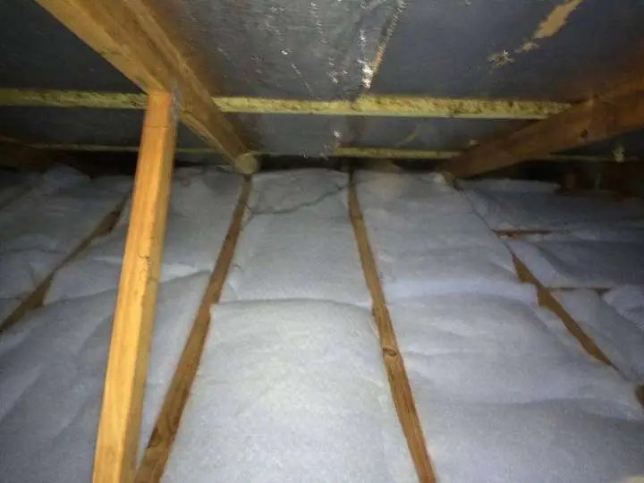 White polyester batts laid between timber ceiling joists under a roof.